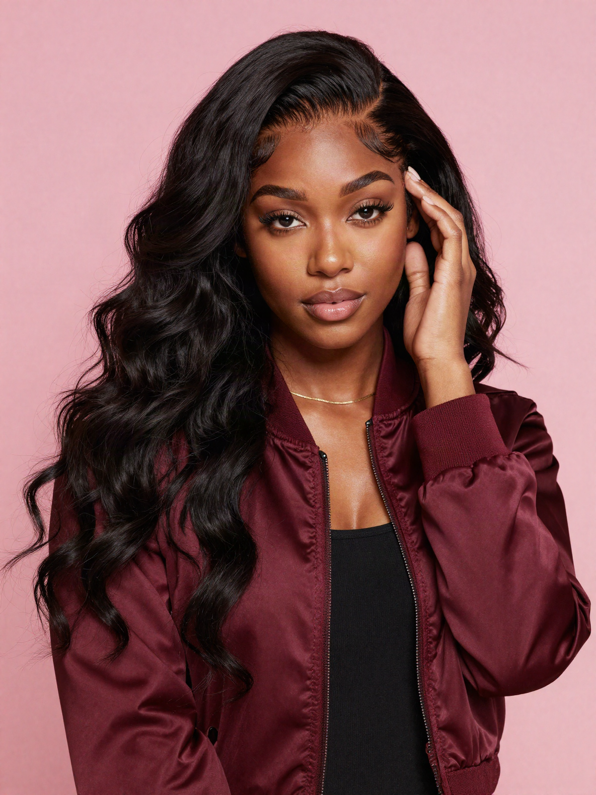 Woman touching the natural hairline of her black loose wave wig on a pink background